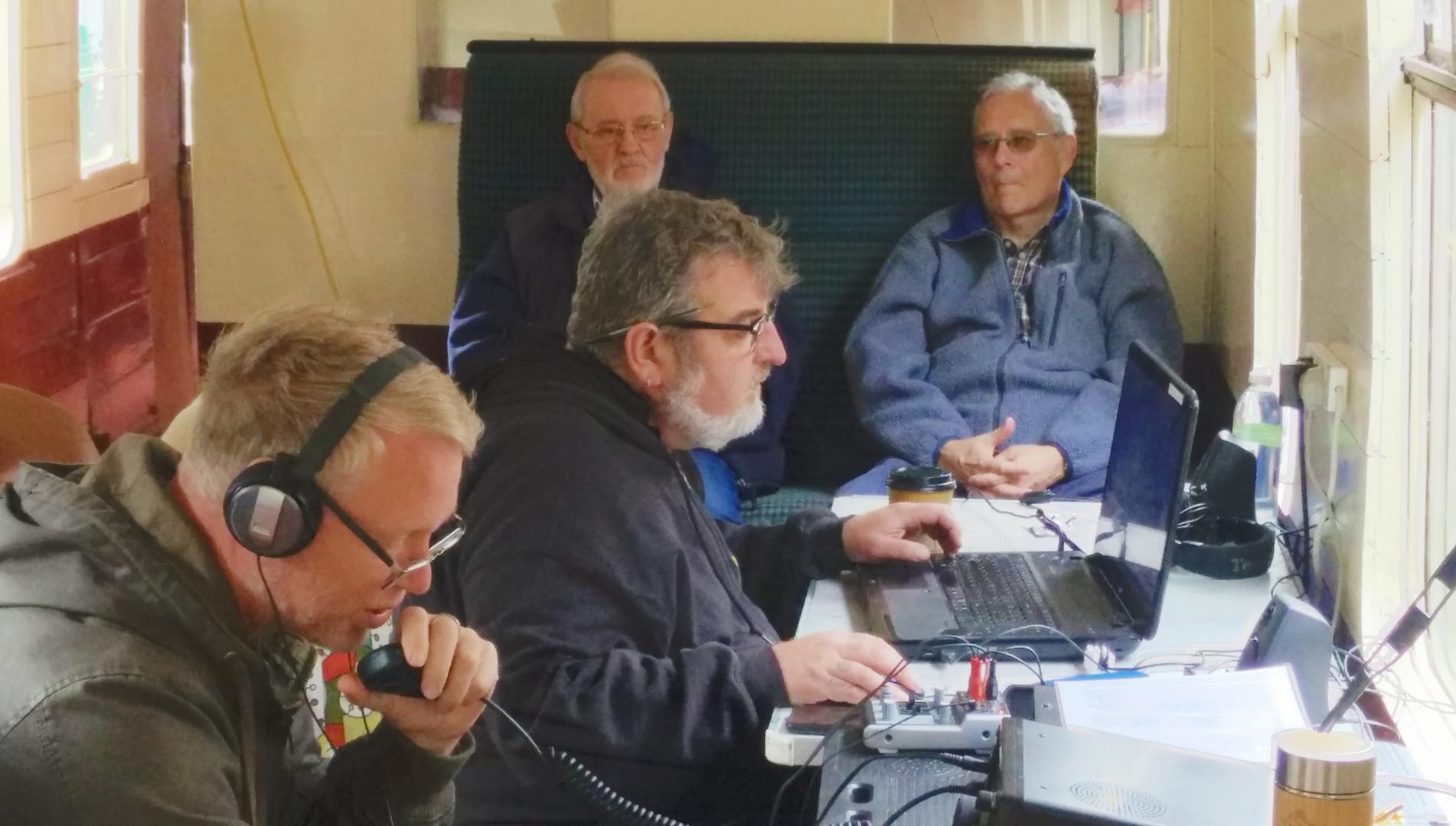 Mark M0SKV operating GB0SDR with Greg 2W1BUF logging. Observing are David M7DVY (right) and Greg's father (left)